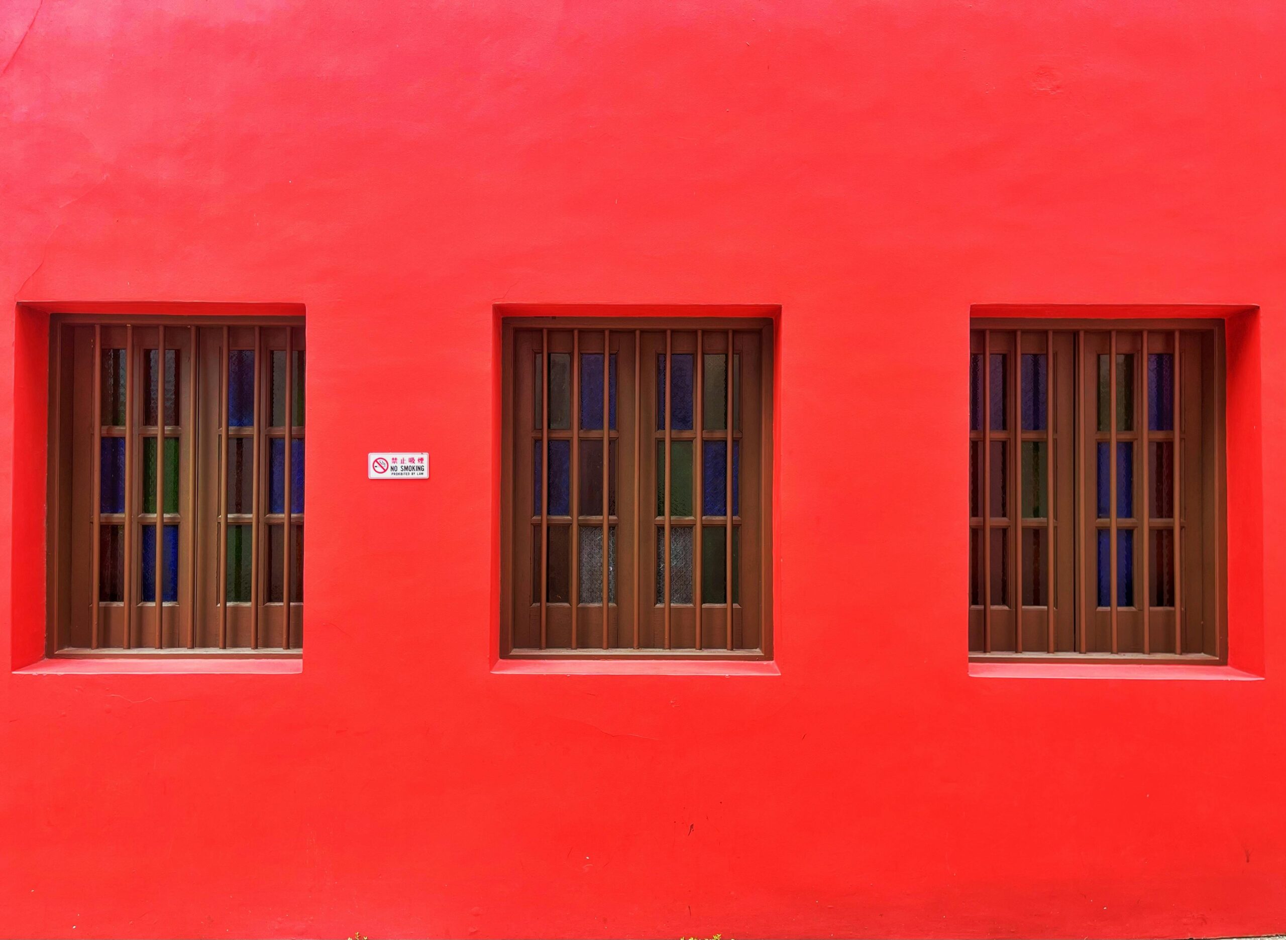 Colorful wall of a building featuring three brown windows, showcasing urban architecture.